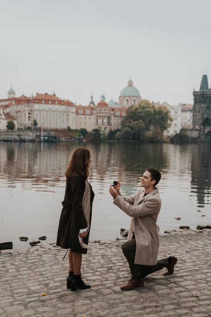 The ring moment beside the Vltava Man holding out a ring while kneeling beside the Vltava during a proposal photoshoot in Prague