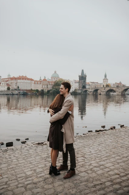 An engagement embrace on the Kampa riverbank Couple hugging on the Kampa riverbank with Prague across the water at their engagement photoshoot