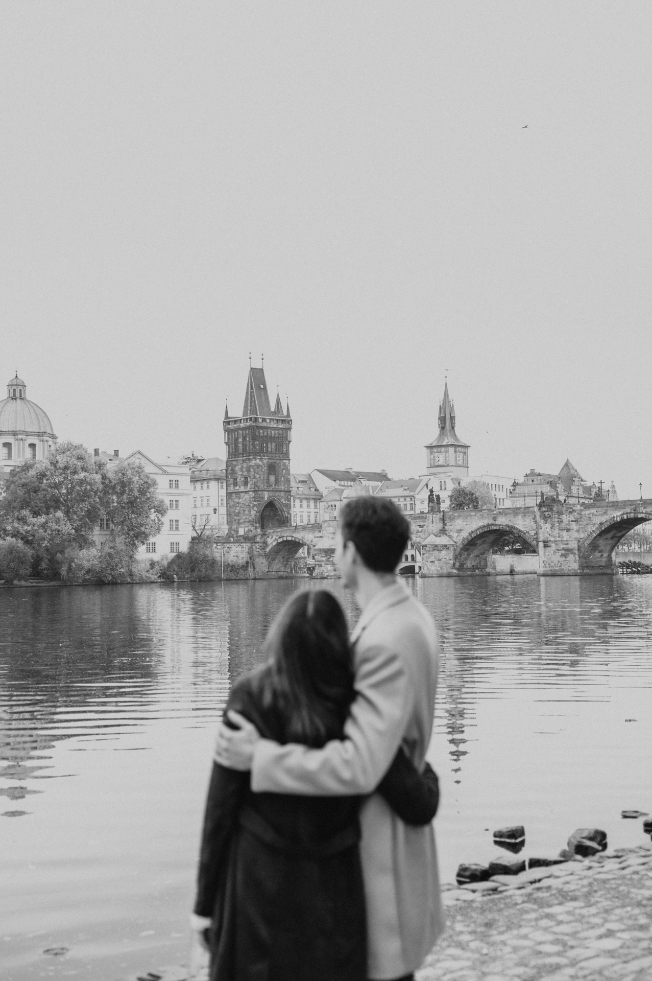 Black and white photograph of the couple looking across the Vltava at their Prague engagement photoshoot