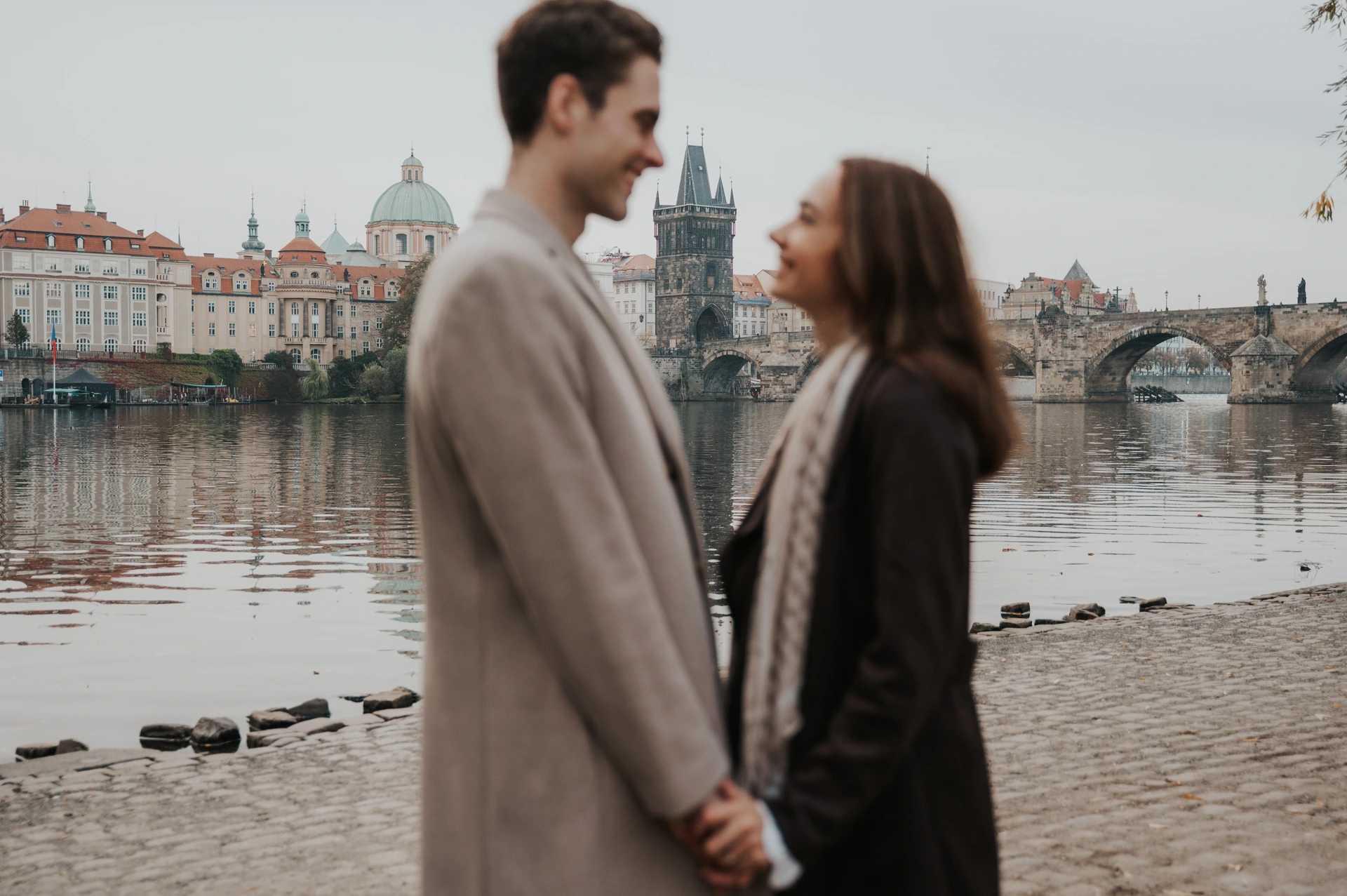 Close landscape portrait of the couple beside the Vltava during their Prague engagement photoshoot