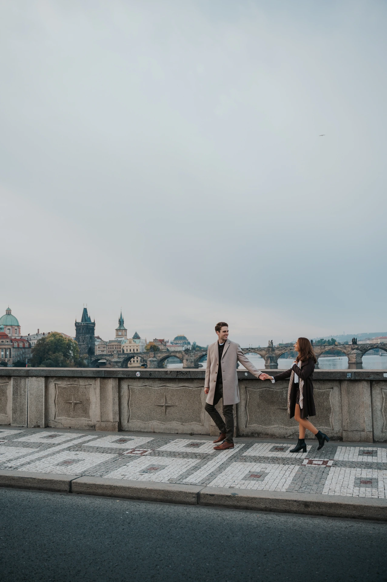 Couple holding hands on patterned riverside pavement during their Prague engagement photoshoot