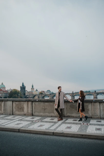 Engagement photoshoot on Prague's riverside paving Couple holding hands on patterned riverside pavement during their Prague engagement photoshoot