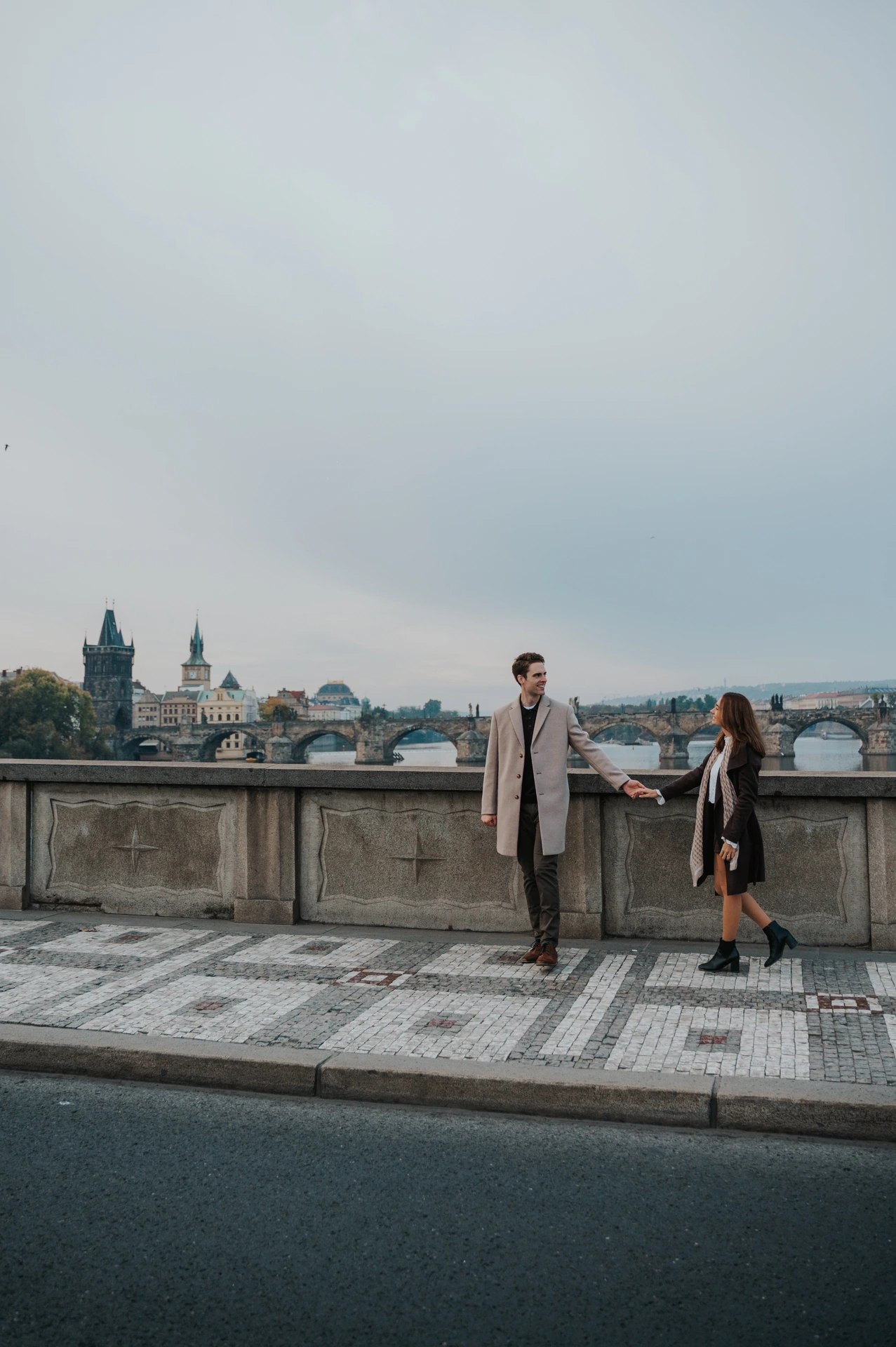 Couple walking hand in hand beside the river during their engagement photoshoot in Prague