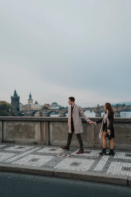 A pause on the Prague riverbank Couple looking towards each other on the riverside pavement during their Prague engagement photoshoot