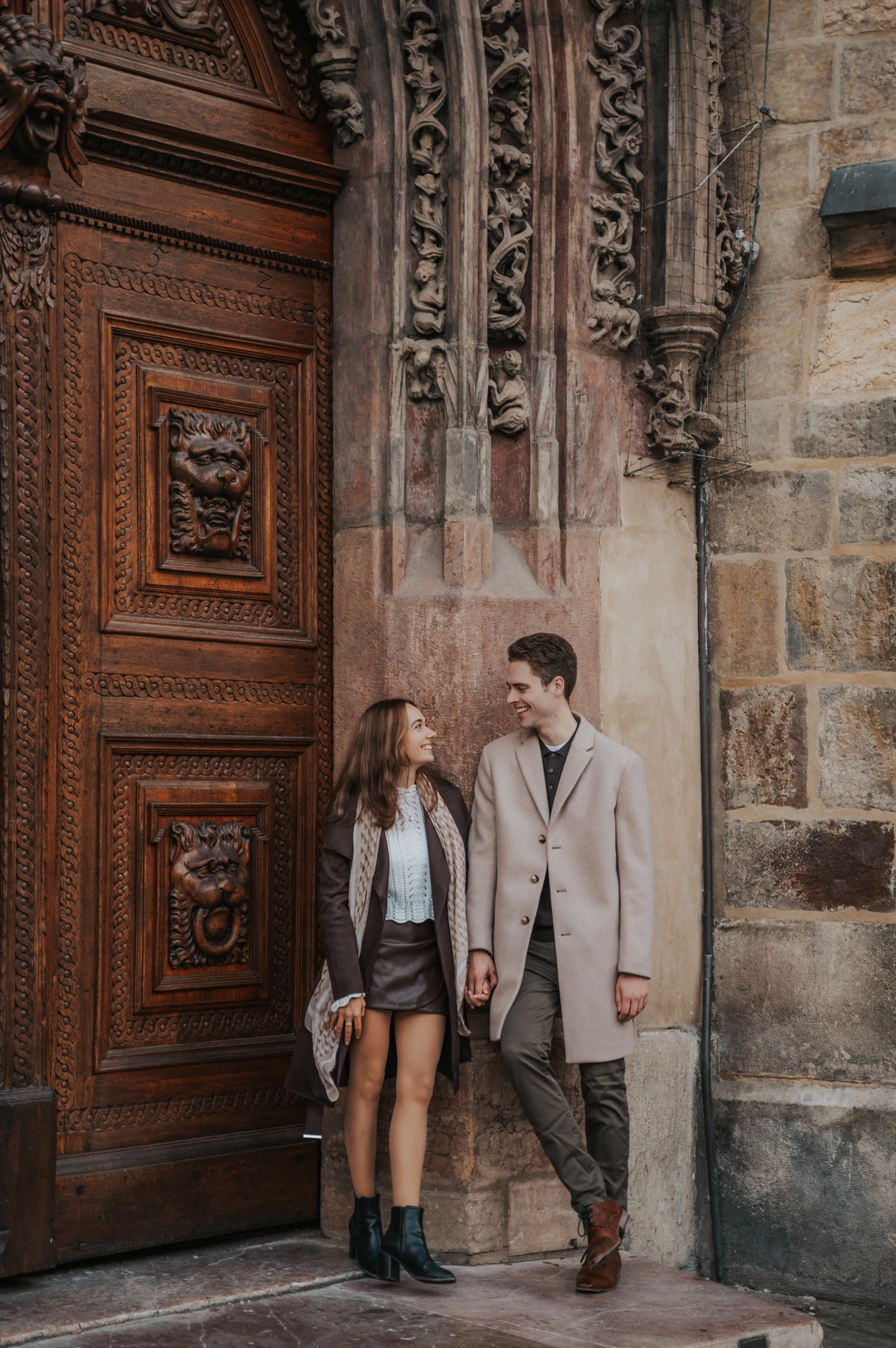 Couple smiling at each other beside a carved wooden doorway during their Prague Old Town engagement photoshoot