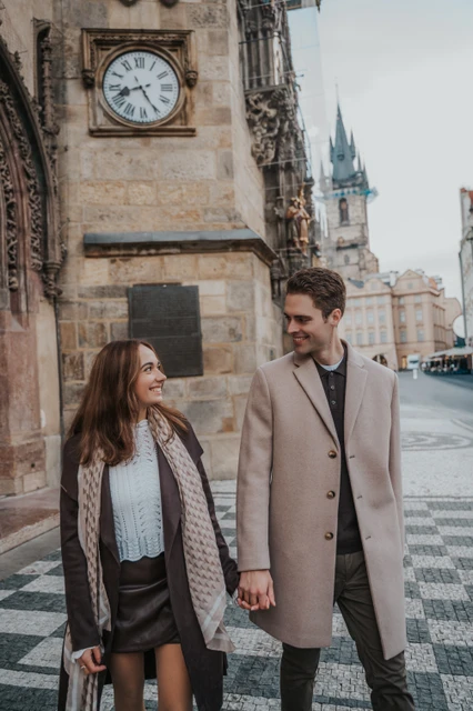 An engagement walk by the Old Town Hall Couple walking hand in hand beside the Old Town Hall during their Prague engagement photoshoot