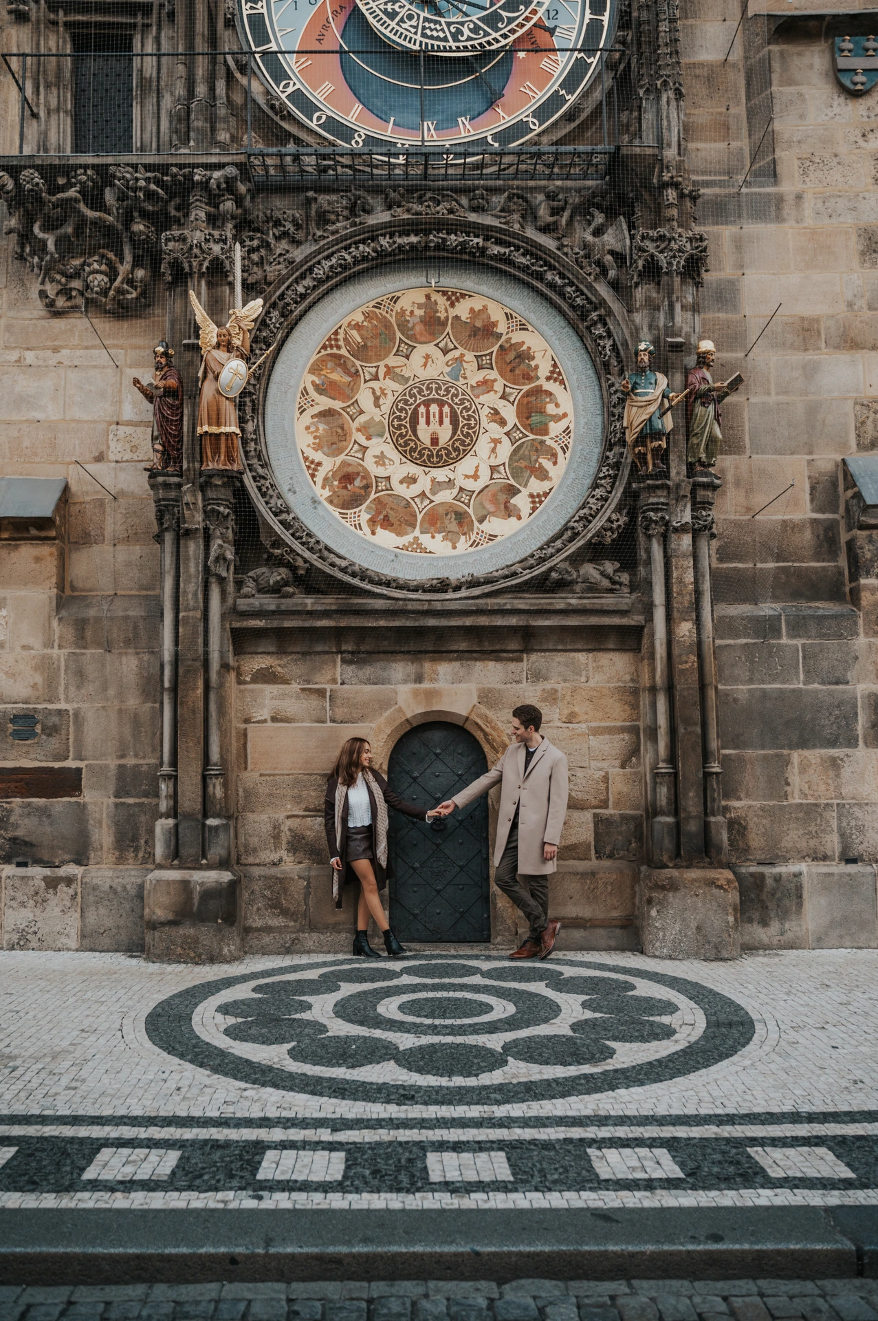 Couple beneath the Astronomical Clock on patterned paving during their Prague engagement photoshoot