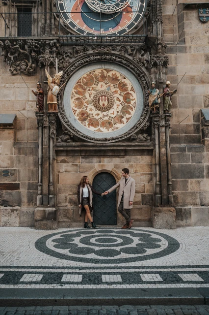 Couple beneath the Astronomical Clock on patterned paving during their Prague engagement photoshoot
