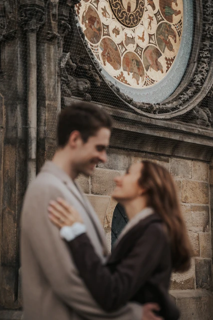 An engagement portrait beneath the clock Close portrait of the couple with the Astronomical Clock behind them during their Prague engagement photoshoot