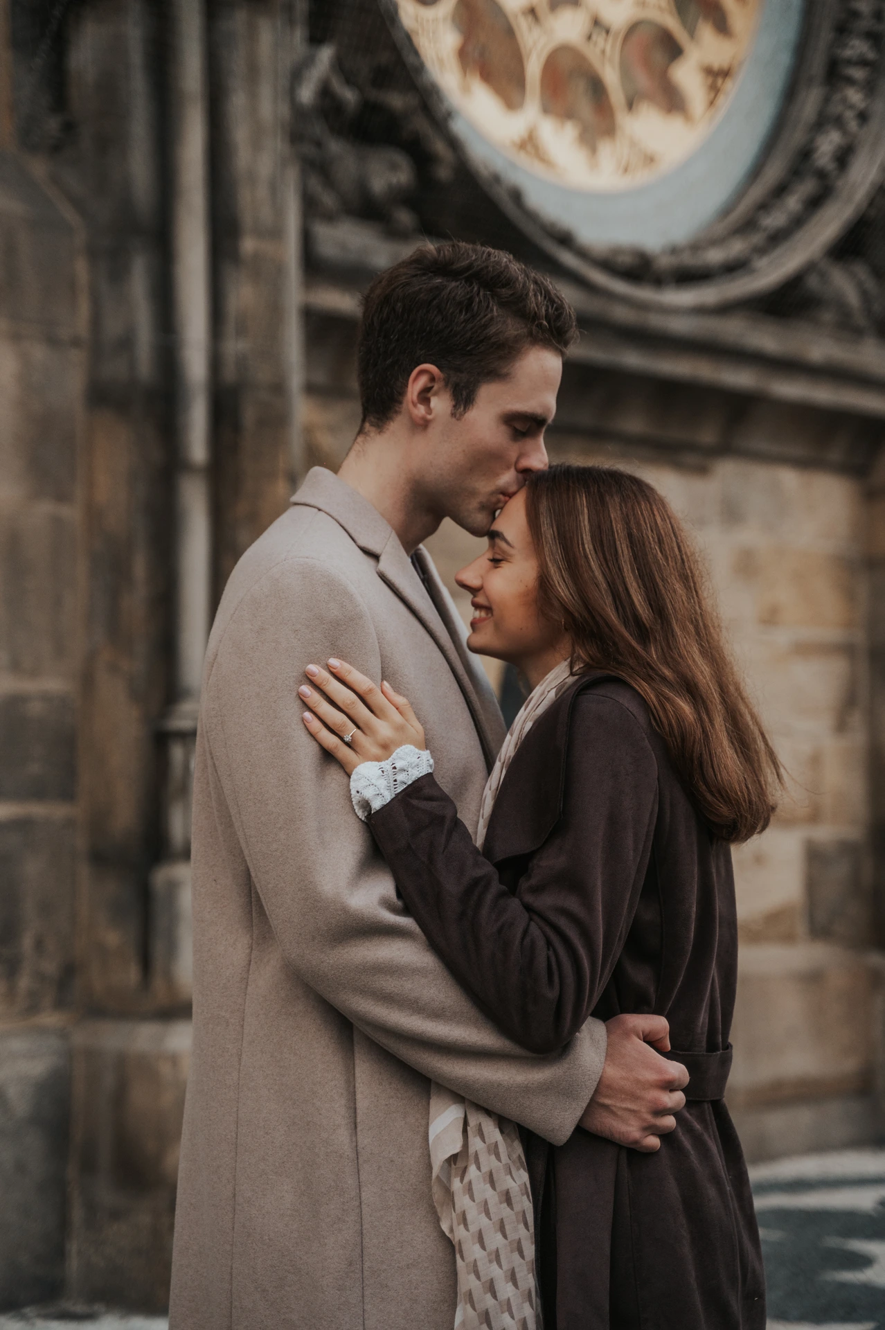 Couple embracing beneath the Astronomical Clock's calendar dial during their engagement photoshoot in Prague