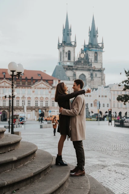 An Old Town Square engagement photoshoot Couple embracing in Old Town Square with the Church of Our Lady before Týn behind them during their Prague engagement photoshoot