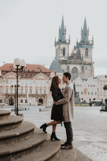 Couple kissing in Old Town Square beneath the twin towers of Týn during their Prague engagement photoshoot