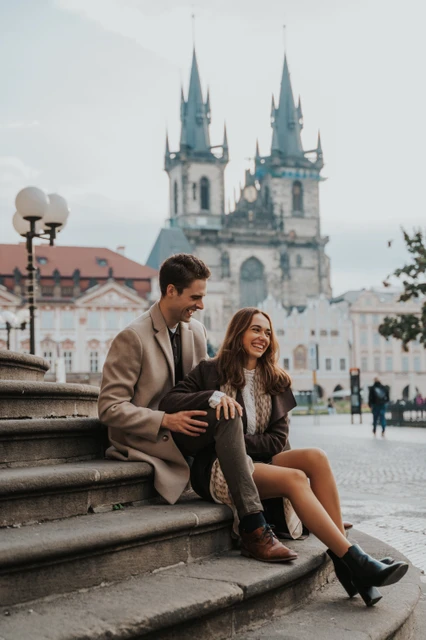 Laughter beneath the Týn towers Couple laughing on steps with the Týn towers behind them during their engagement photoshoot in Prague