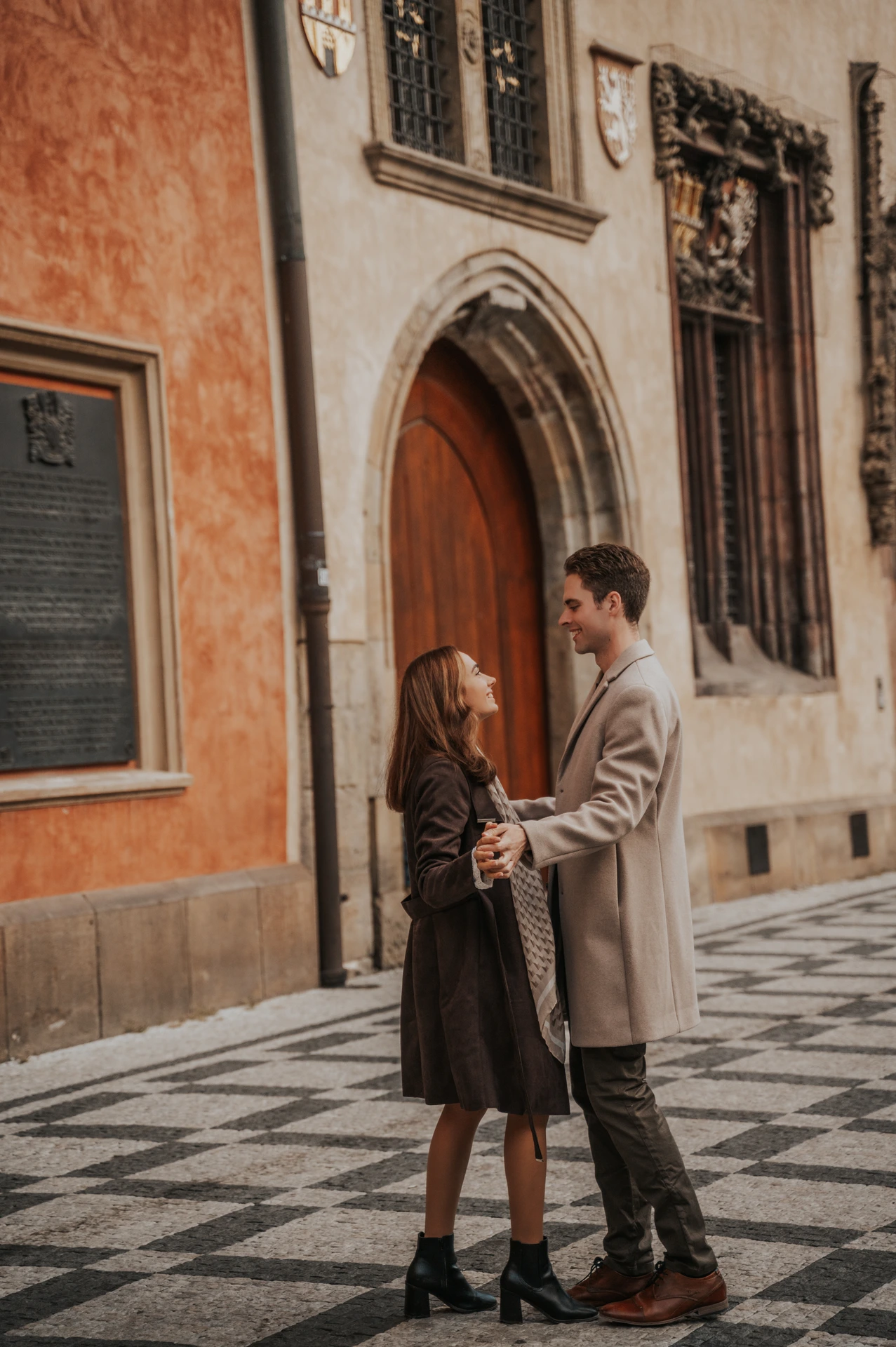 Couple holding hands beside warm-coloured façades during their engagement photoshoot in Prague Old Town