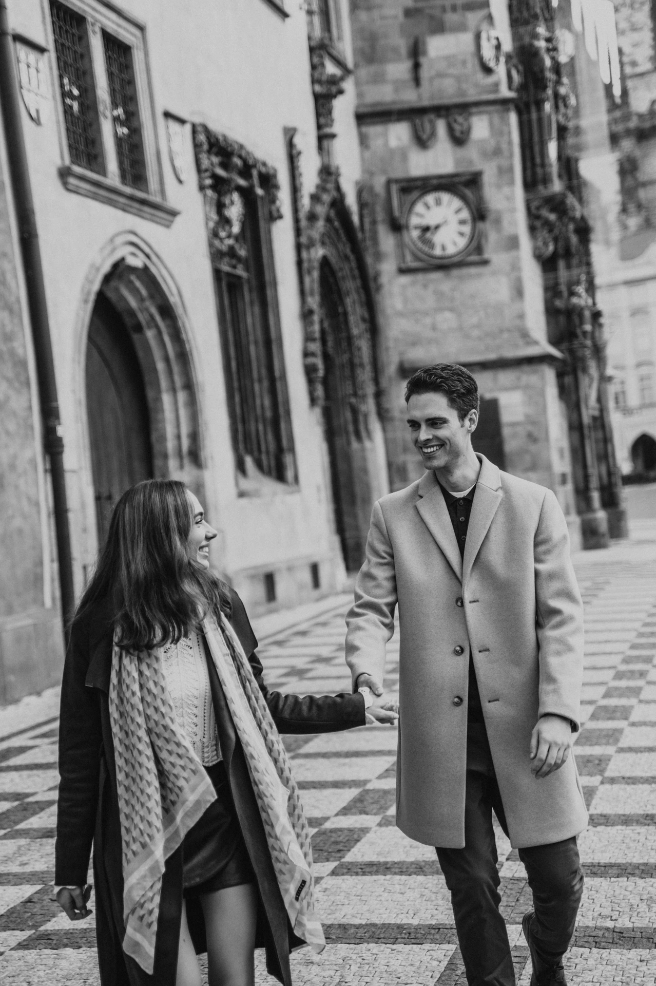 Black and white photograph of the couple walking through Old Town during their Prague engagement photoshoot