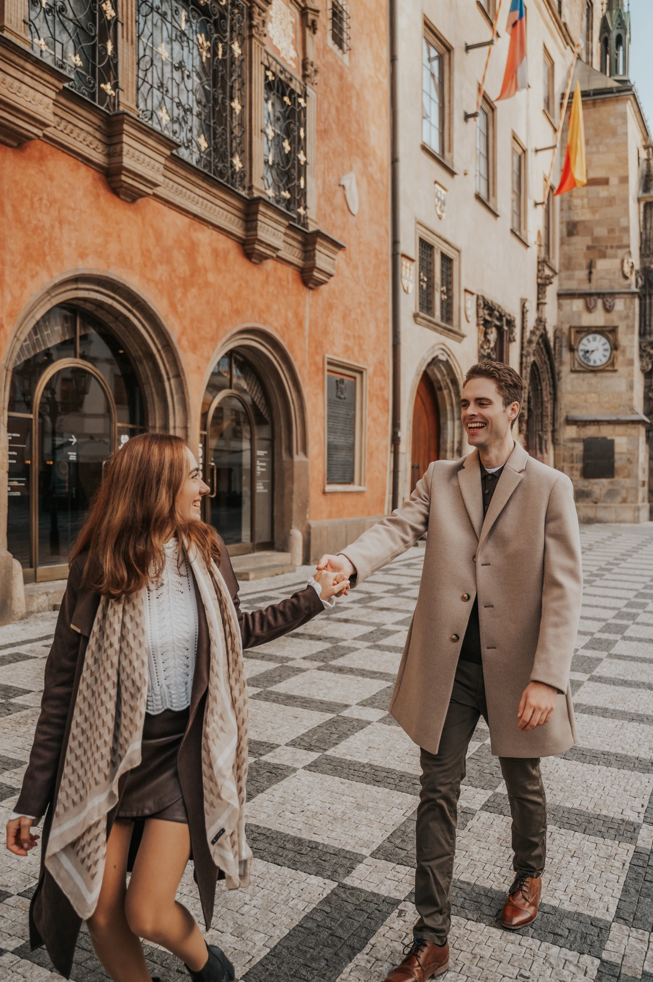 Couple smiling at each other beside an orange façade during their Prague Old Town engagement photoshoot