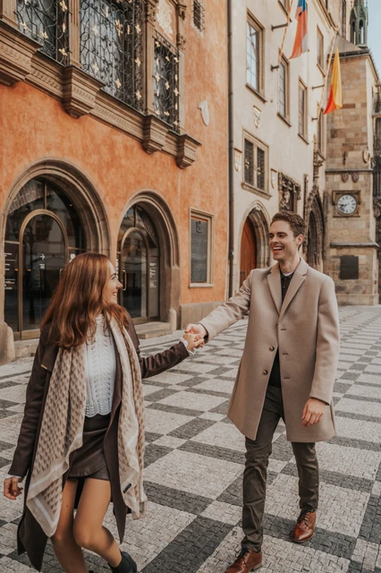 Smiles beside an orange Old Town façade Couple smiling at each other beside an orange façade during their Prague Old Town engagement photoshoot