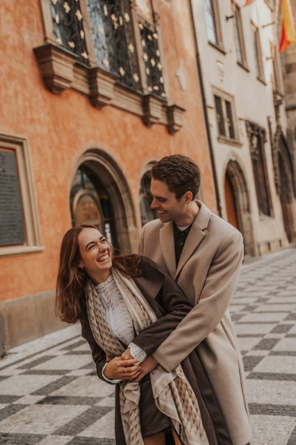 Laughter on their Prague engagement photoshoot Woman laughing while her fiancé embraces her in an Old Town street during their Prague engagement photoshoot