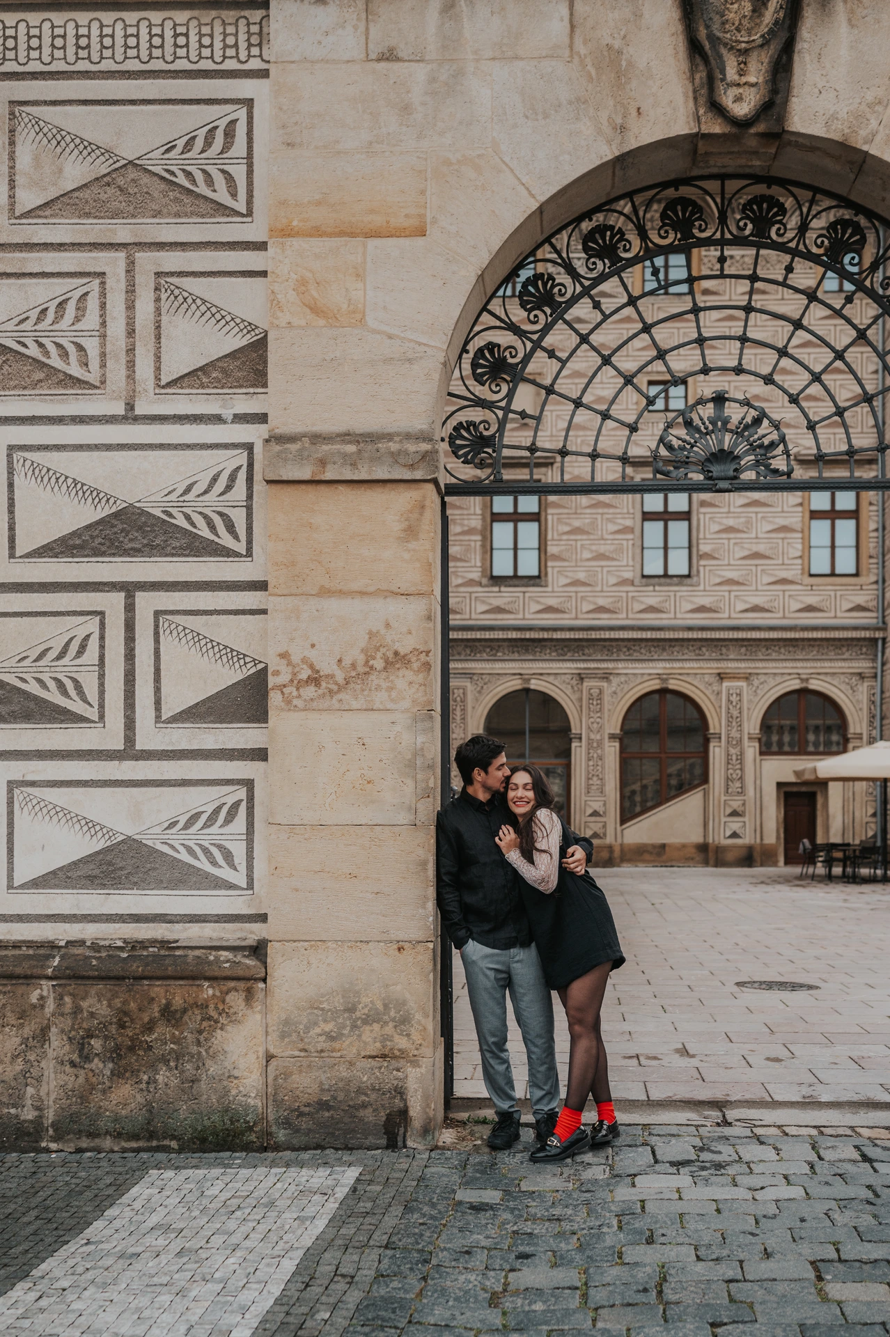 Man kissing his partner beside an arched iron gateway during the couple's engagement photoshoot around Prague Castle.
