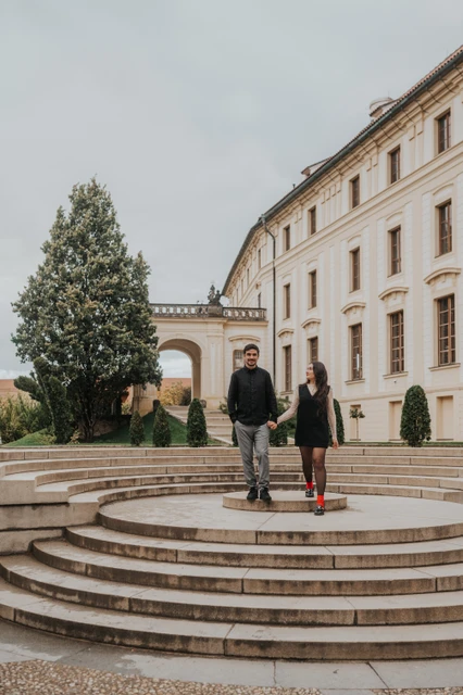 Prague engagement photoshoot on the curved castle courtyard steps Couple standing together on broad curved steps in a castle courtyard during their Prague engagement photoshoot.
