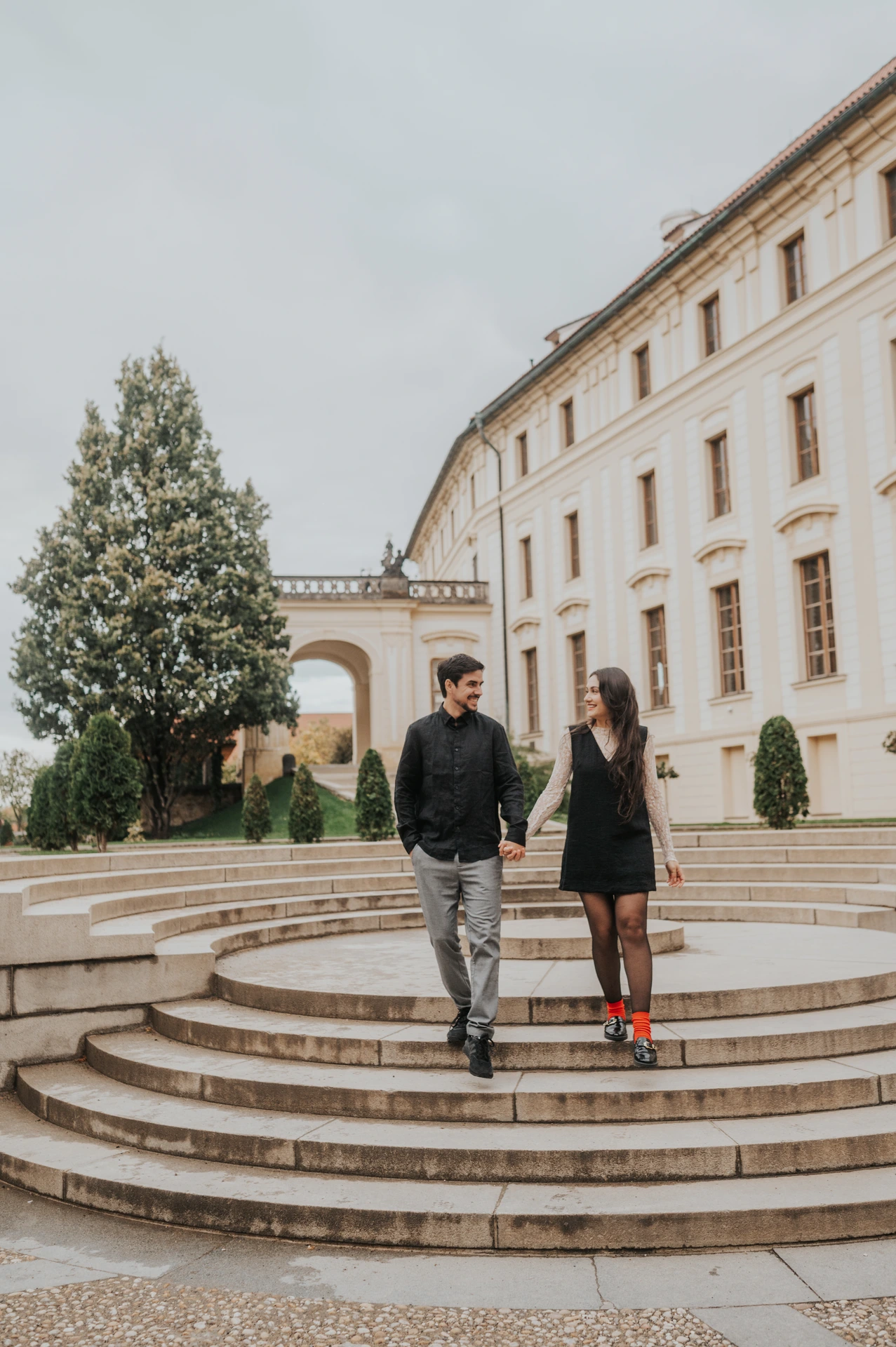 Couple looking towards each other while walking down the curved courtyard steps during their engagement photoshoot at Prague Castle.