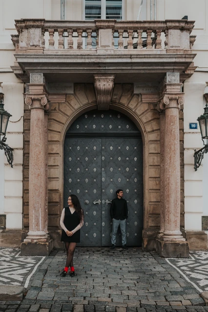 Prague engagement photoshoot at a grand studded doorway Couple standing apart in front of a tall studded door and carved stone doorway during their Prague engagement photoshoot.