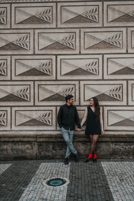 Prague engagement photoshoot beside the patterned castle wall Newly engaged couple holding hands beside a geometrically patterned wall during their engagement photoshoot in Prague.