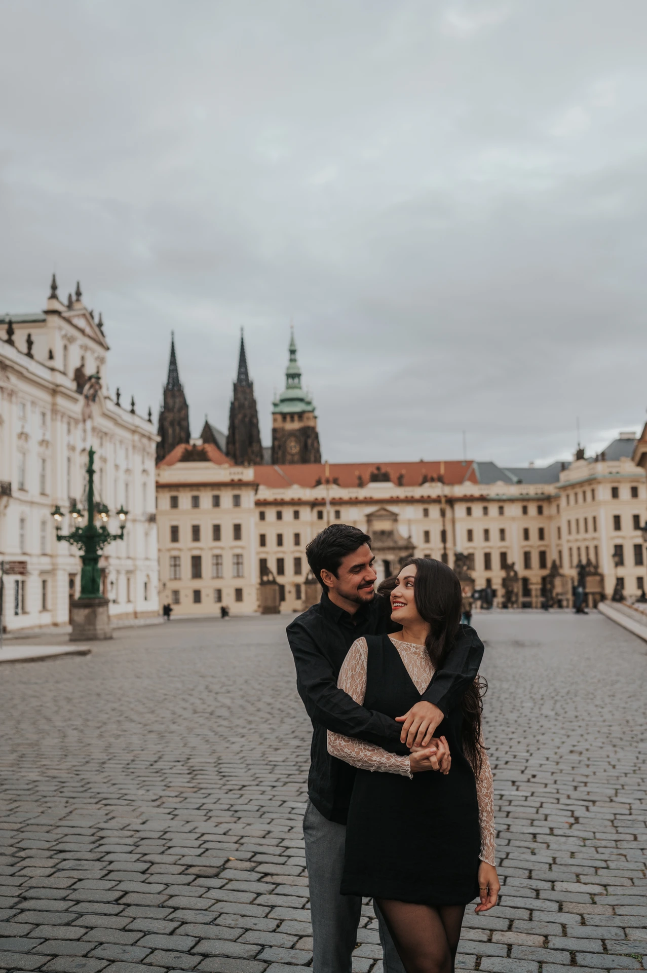 Couple sharing a close embrace in the square with cathedral spires behind them during their engagement photoshoot in Prague.