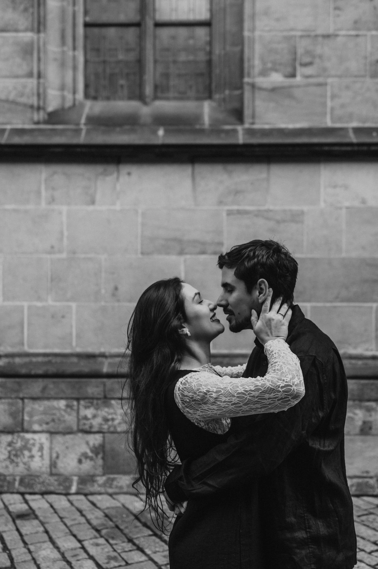 Black-and-white close portrait of the couple kissing beside the cathedral wall during their Prague engagement photoshoot.