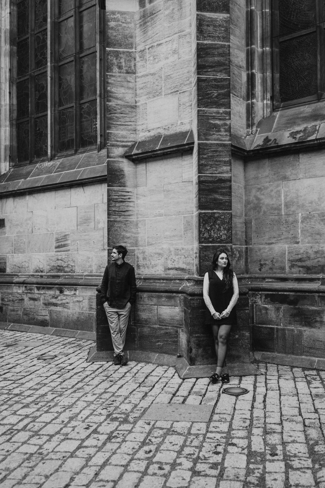 Black-and-white full-length portrait of the couple beside the cathedral stone wall during their Prague engagement photoshoot.