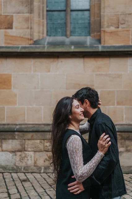 Prague engagement photoshoot with a close embrace by the cathedral wall Couple holding each other close beside the stone cathedral wall during their engagement photoshoot in Prague.