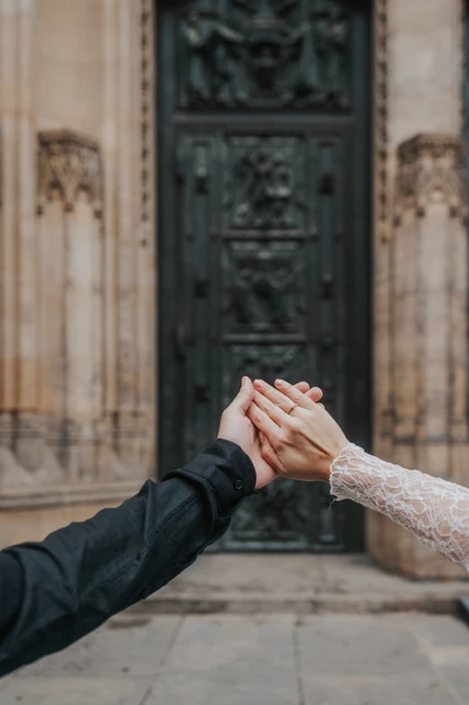 Couple holding their hands up to show the engagement ring, with the cathedral door behind them, during their Prague engagement photoshoot.