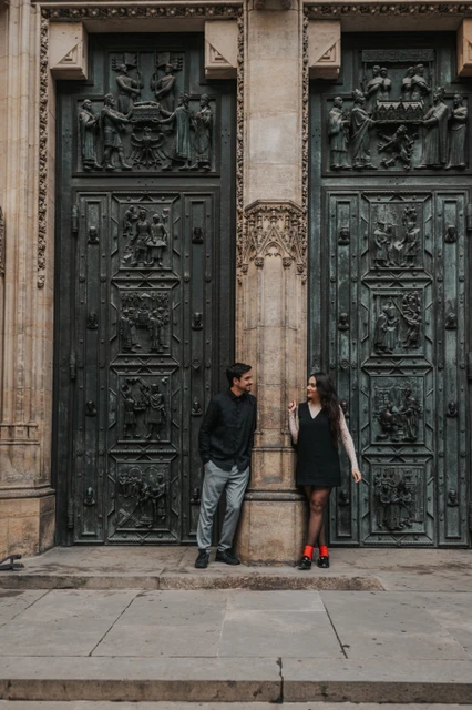 Couple standing either side of a stone column between the bronze St. Vitus Cathedral doors during their Prague engagement photoshoot.