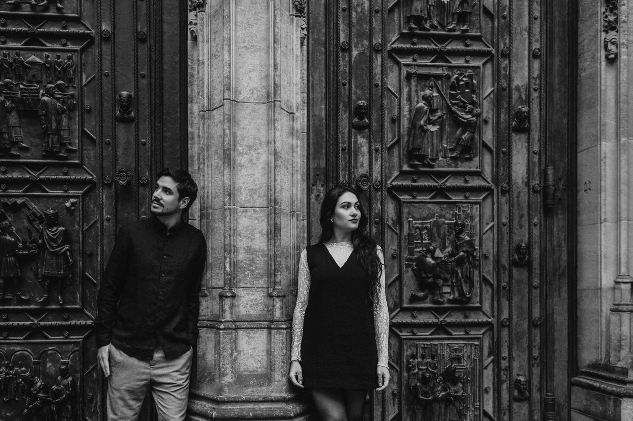 Prague engagement photoshoot at the cathedral doors in black and white Black-and-white landscape portrait of the couple beside the bronze cathedral doors during their Prague engagement photoshoot.