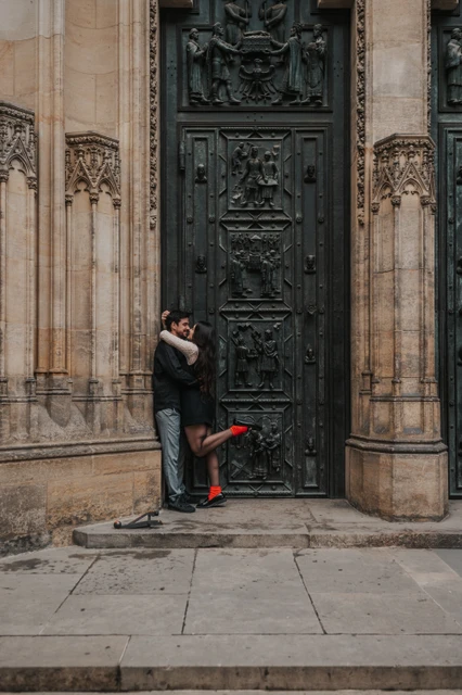 Prague engagement photoshoot with a kiss at St. Vitus Cathedral Couple kissing by the St. Vitus Cathedral doorway, with her red boot lifted behind her, during their engagement photoshoot in Prague.
