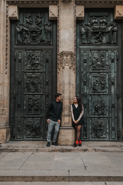 Prague engagement photoshoot with a smile by the cathedral doors Couple smiling towards each other in front of the decorated St. Vitus Cathedral doors during their engagement photoshoot in Prague.