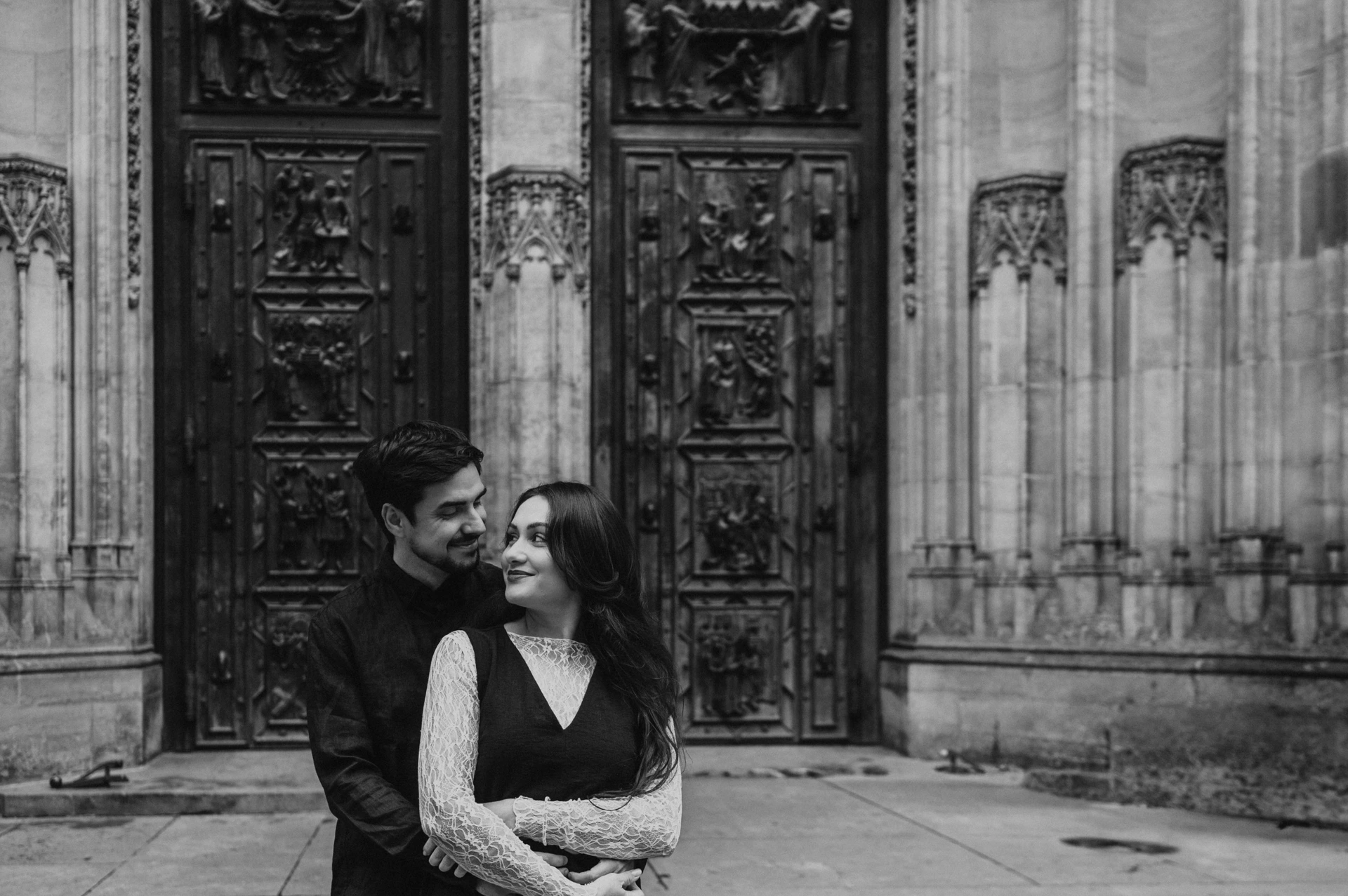 Black-and-white landscape portrait of the couple embracing beside St. Vitus Cathedral during their Prague engagement photoshoot.