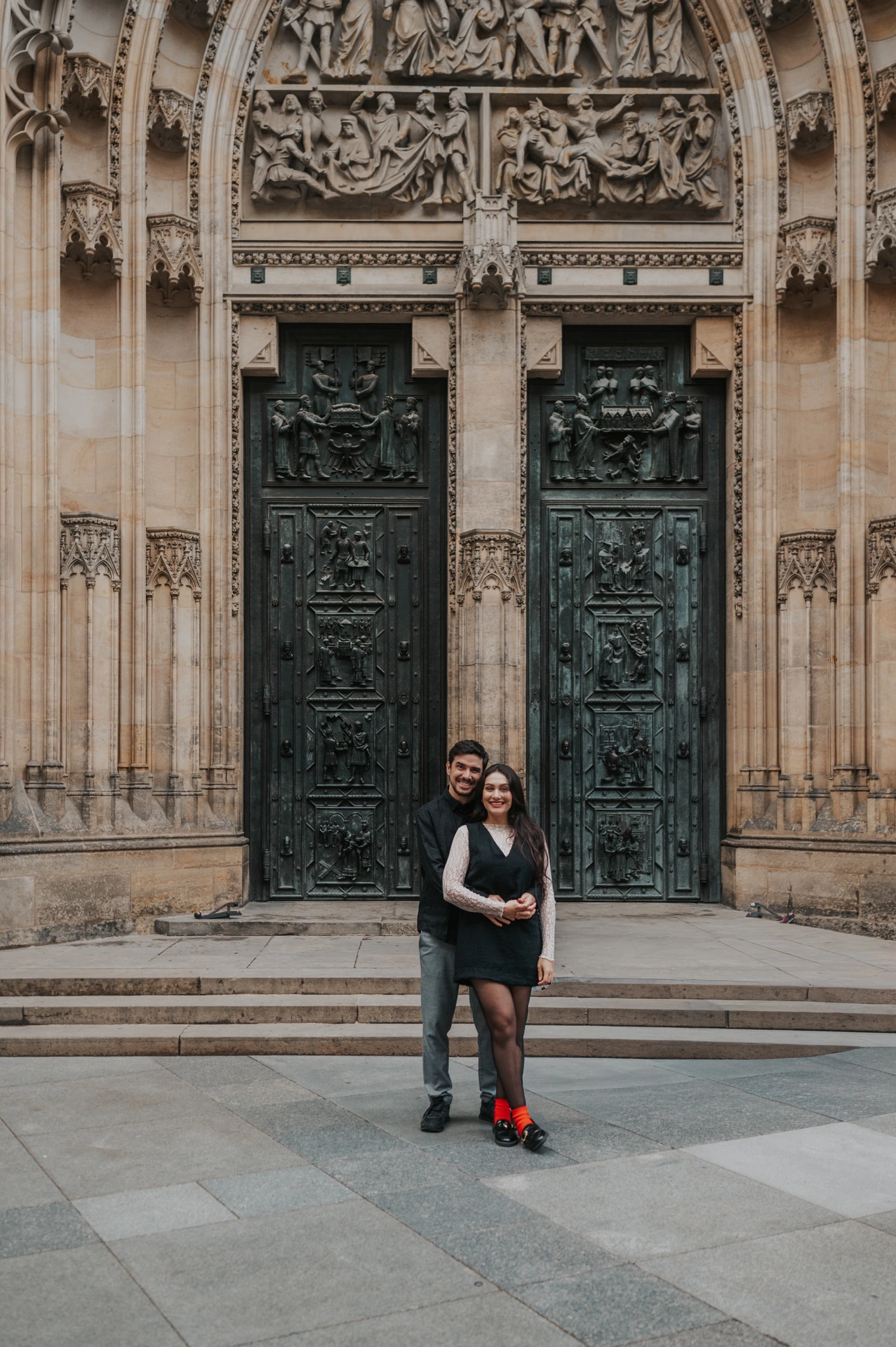 Couple embracing beneath the carved Gothic portal of St. Vitus Cathedral during their Prague engagement photoshoot.