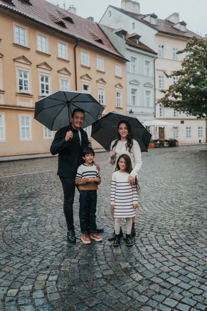 Parents and their twins standing together beneath umbrellas on wet cobblestones in Kampa during their Prague family photoshoot.