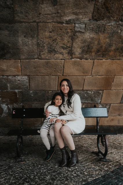 Mother and daughter sitting close together on a bench beneath Charles Bridge during their Prague family photoshoot.