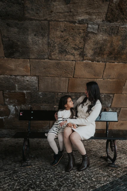 Prague family photoshoot: a shared look between mother and daughter Mother and daughter looking at each other while seated on the bench below Charles Bridge during their Prague family photoshoot.