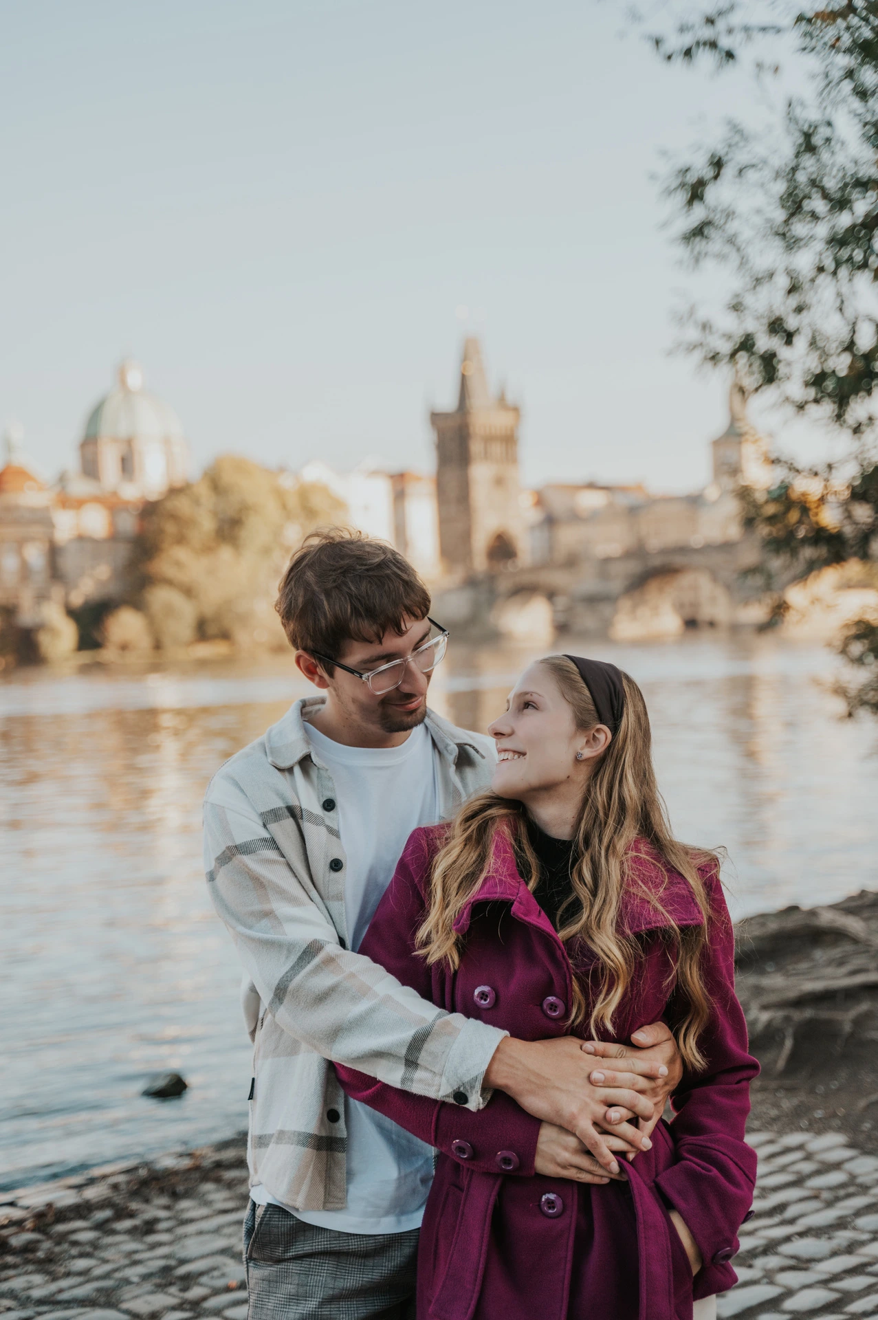 Couple embracing with Charles Bridge across the water during a couple photoshoot in Prague.