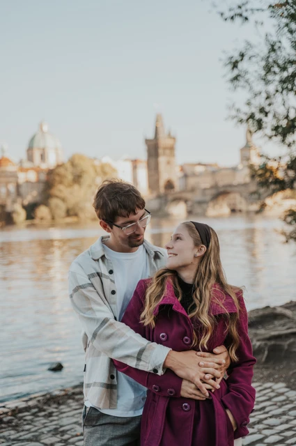 Prague couple photoshoot: couple embracing with Charles Bridge across the water. Couple embracing with Charles Bridge across the water during a couple photoshoot in Prague.