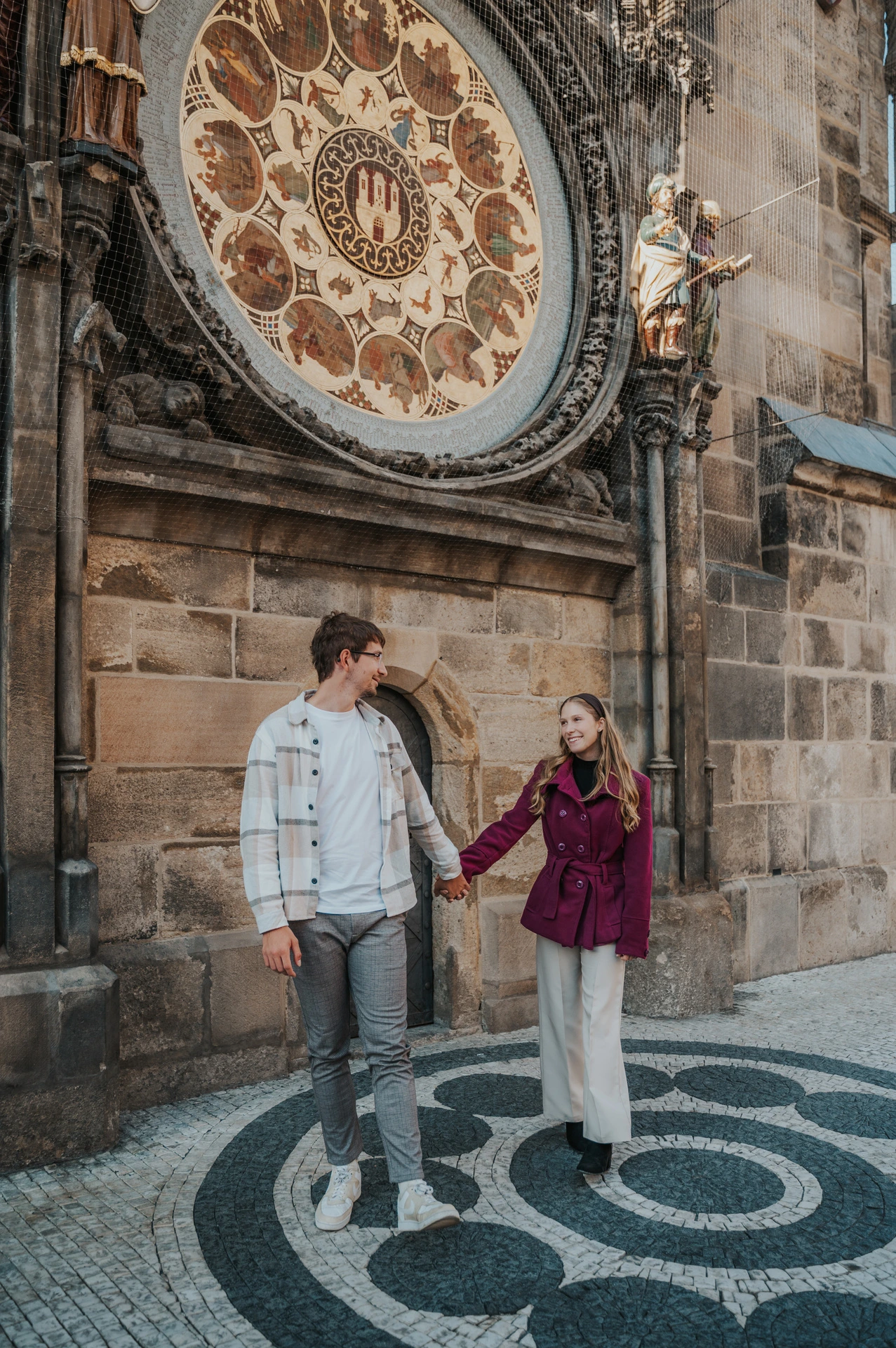 Couple holding hands on the patterned pavement by the clock during a couple photoshoot in Prague.