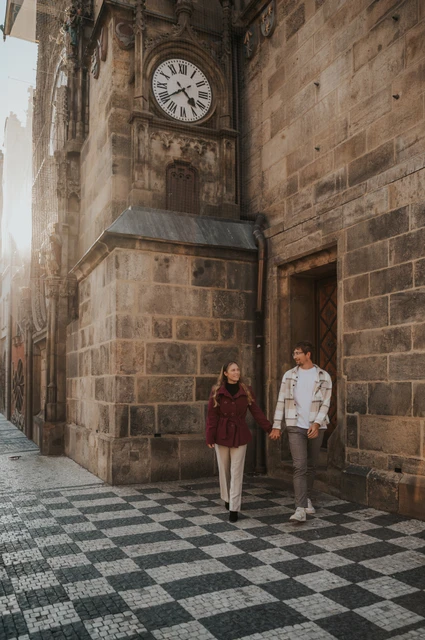 Prague couple photoshoot: couple holding hands under the small Old Town clock. Couple holding hands under the small Old Town clock during a couple photoshoot in Prague.