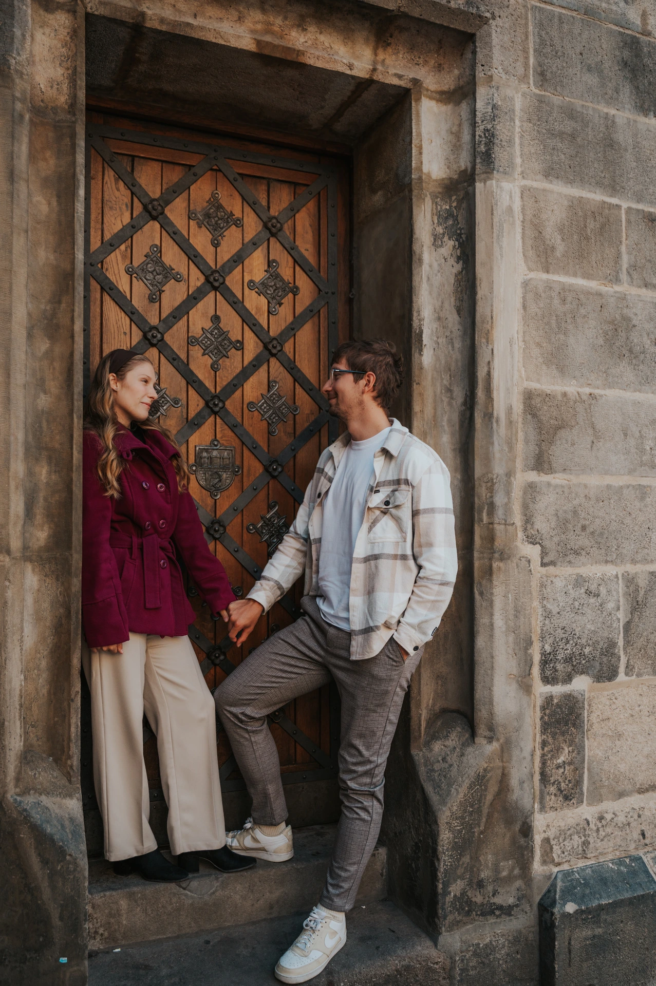 Couple pausing beside a patterned wooden door during a couple photoshoot in Prague.