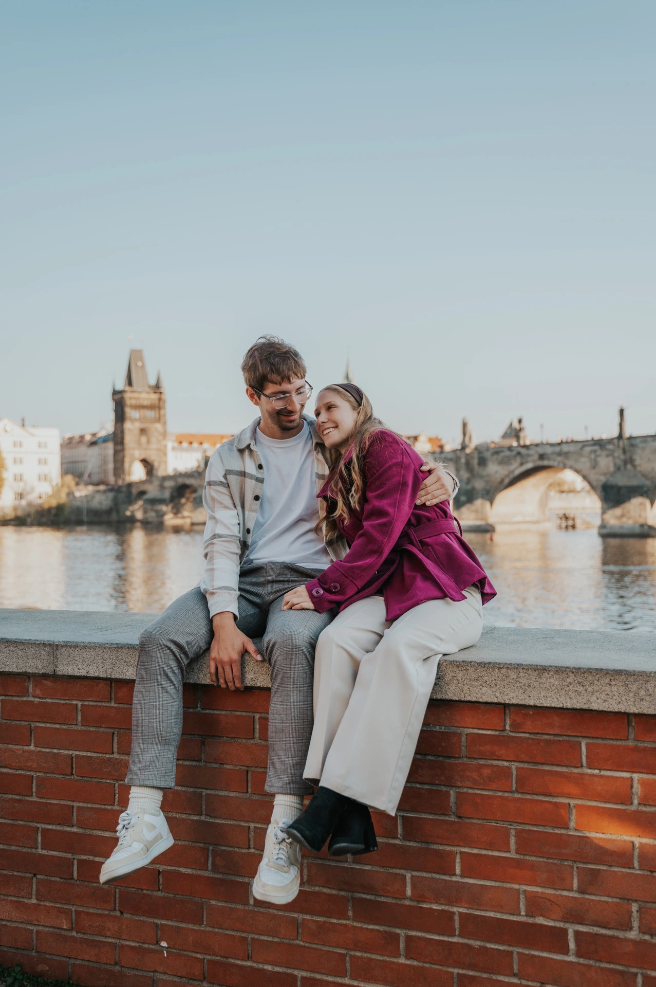 Couple sitting on a riverside wall overlooking the Vltava during a couple photoshoot in Prague.
