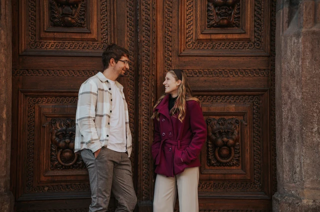 Couple smiling at each other beside carved wooden doors during a couple photoshoot in Prague.