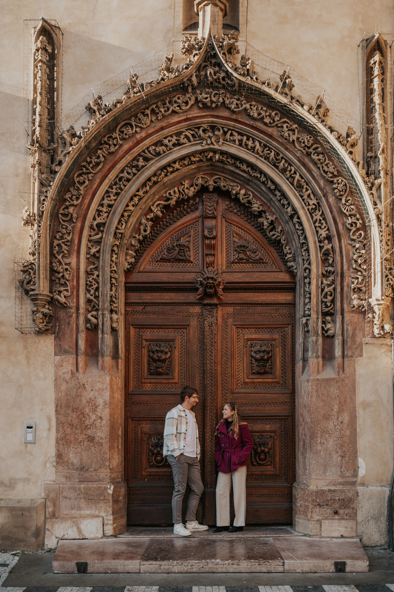 Couple standing at an ornate wooden entrance in Old Town during a couple photoshoot in Prague.