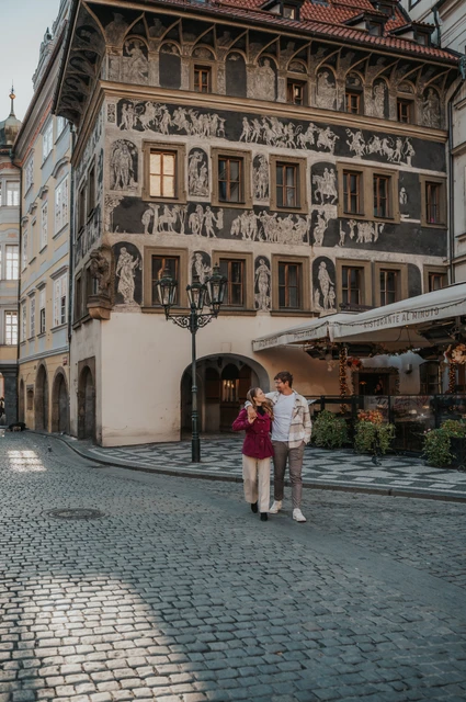 Prague couple photoshoot: couple standing in front of a painted Old Town facade. Couple standing in front of a painted Old Town facade during a couple photoshoot in Prague.